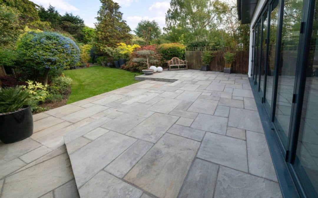 A stone patio with a large glass door, surrounded by a beautifully maintained garden space.